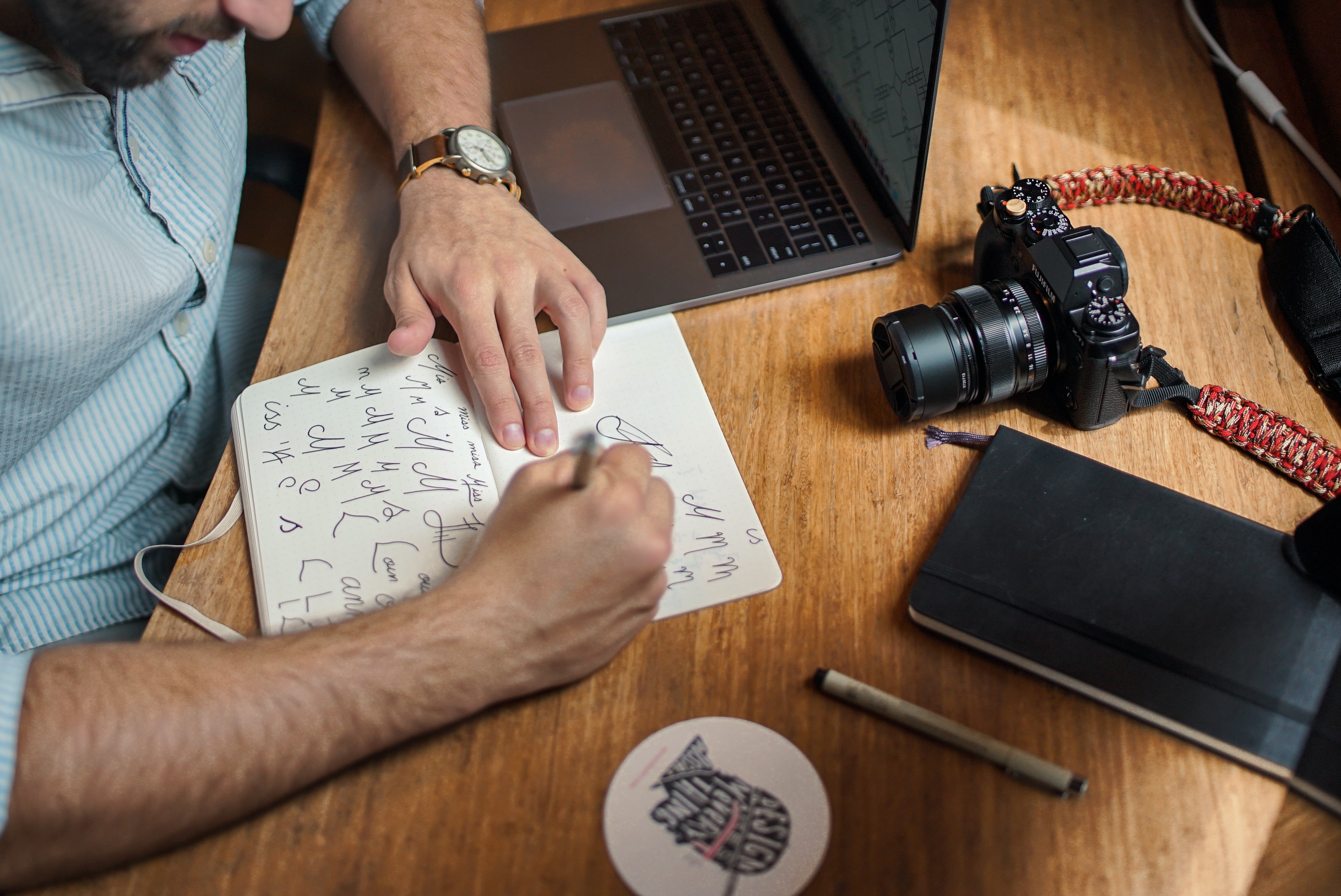 Homme en train de concevoir un logo, dessinant des idées sur papier à son bureau avec un ordinateur portable, un appareil photo et un carnet dans un environnement créatif.